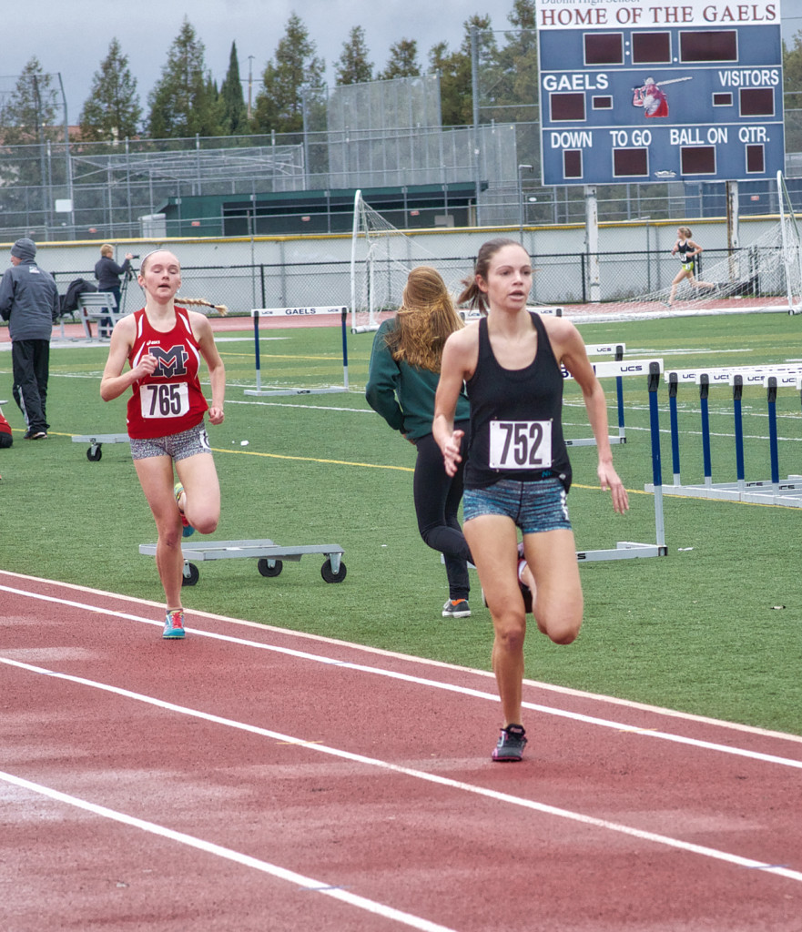 Athlete prepares for pole vault on a track with others watching.