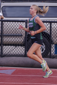 Athlete prepares for pole vault on a track with others watching.