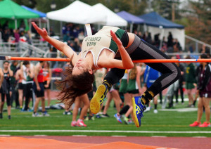 Athlete prepares for pole vault on a track with others watching.