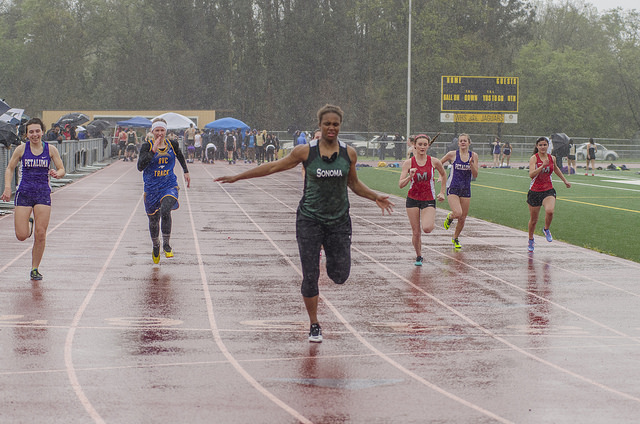 Athlete prepares for pole vault on a track with others watching.