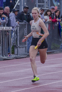 Athlete prepares for pole vault on a track with others watching.