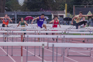 Athlete prepares for pole vault on a track with others watching.