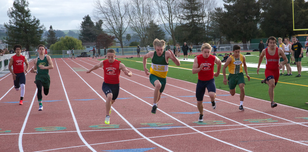 Athlete prepares for pole vault on a track with others watching.