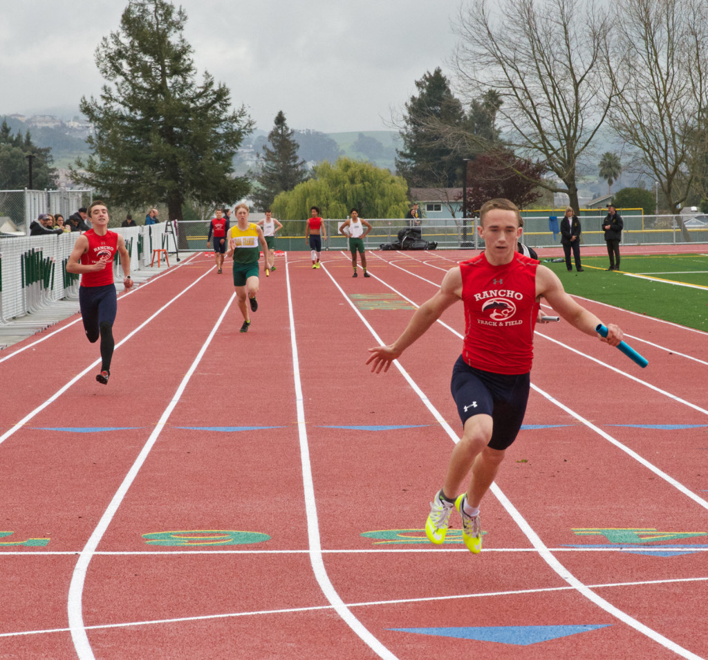 Athlete prepares for pole vault on a track with others watching.
