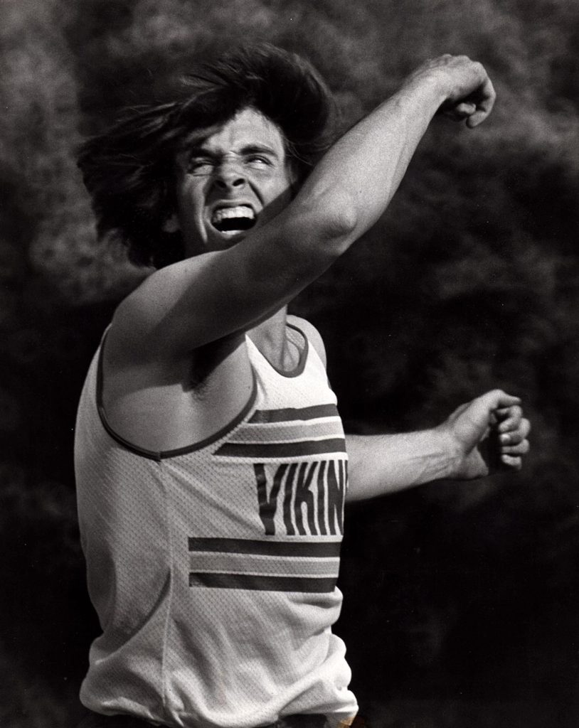 Athlete prepares for pole vault on a track with others watching.