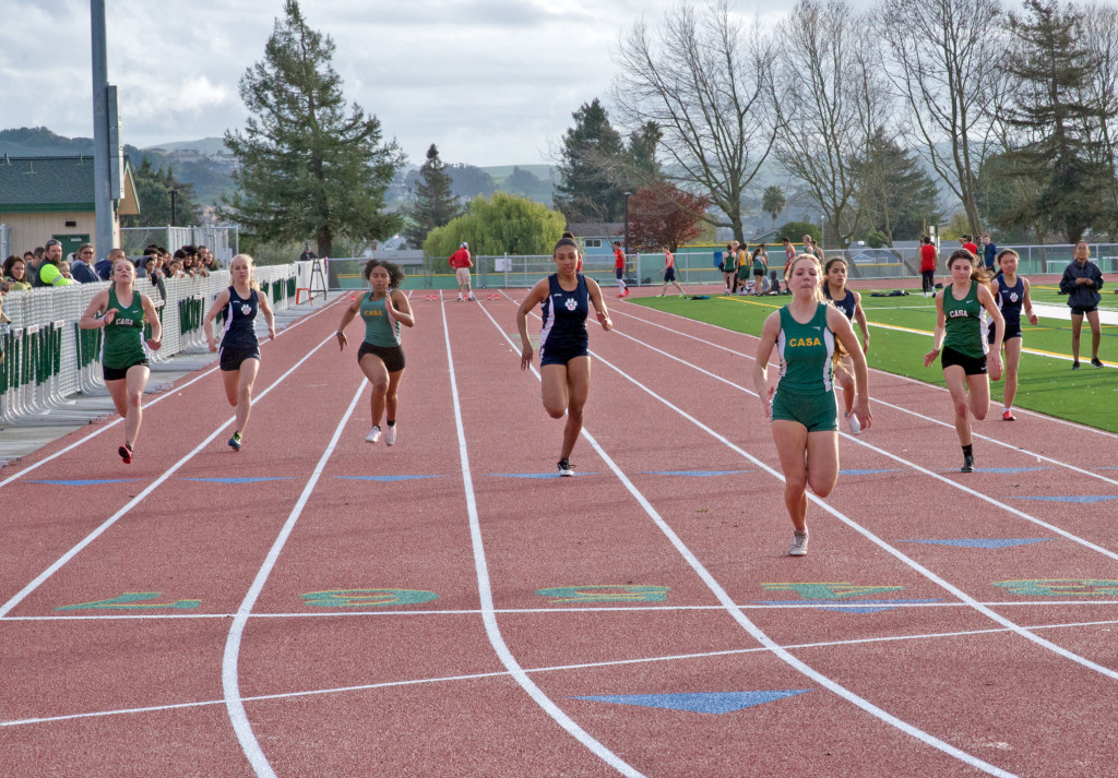 Athlete prepares for pole vault on a track with others watching.