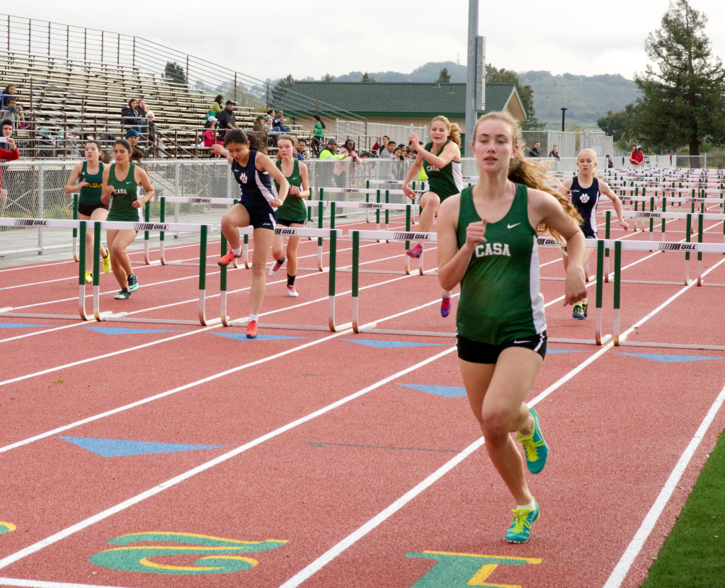 Athlete prepares for pole vault on a track with others watching.