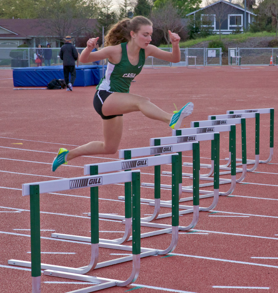 Athlete prepares for pole vault on a track with others watching.