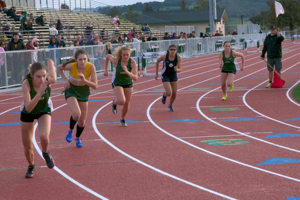 Athlete prepares for pole vault on a track with others watching.