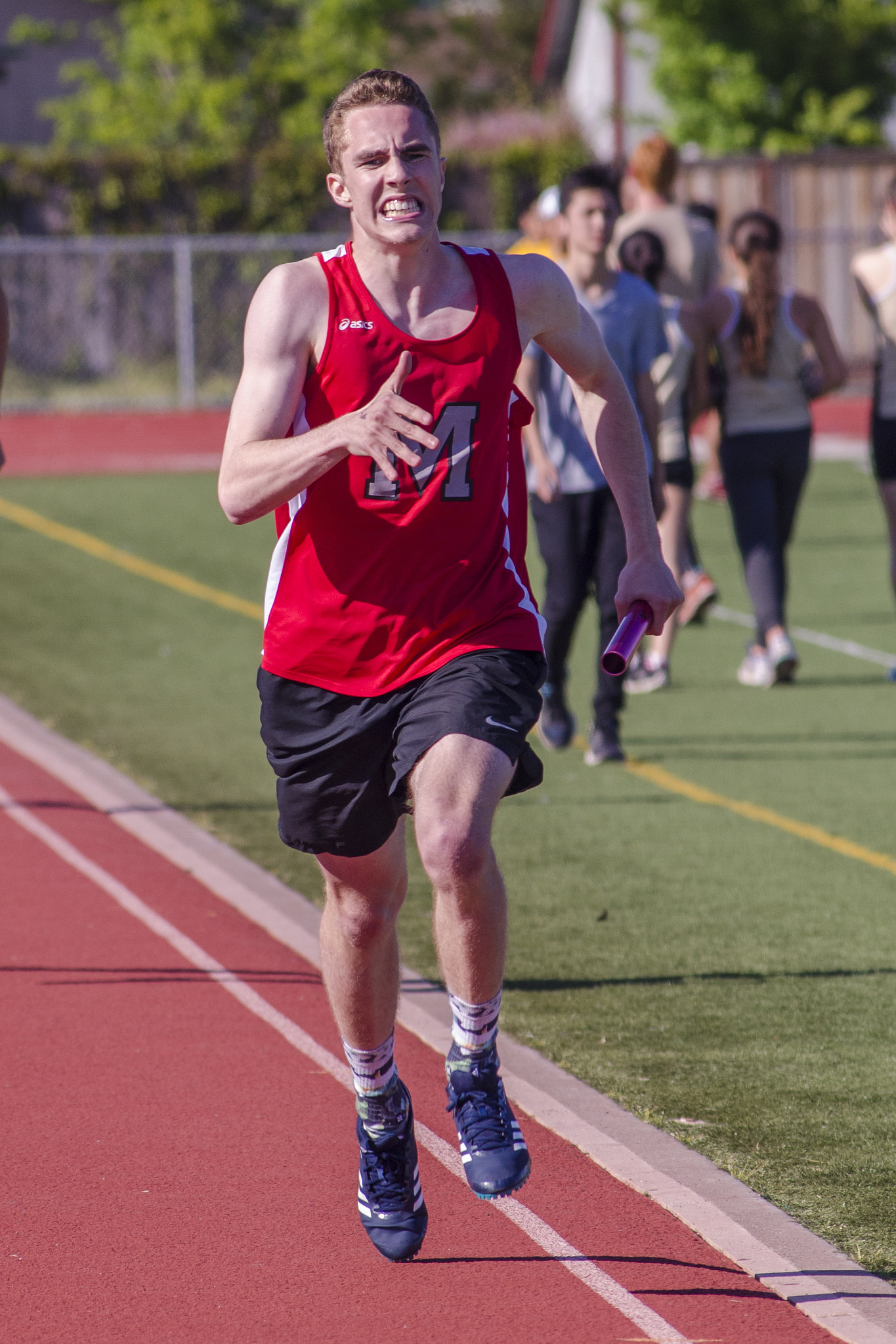 Athlete prepares for pole vault on a track with others watching.