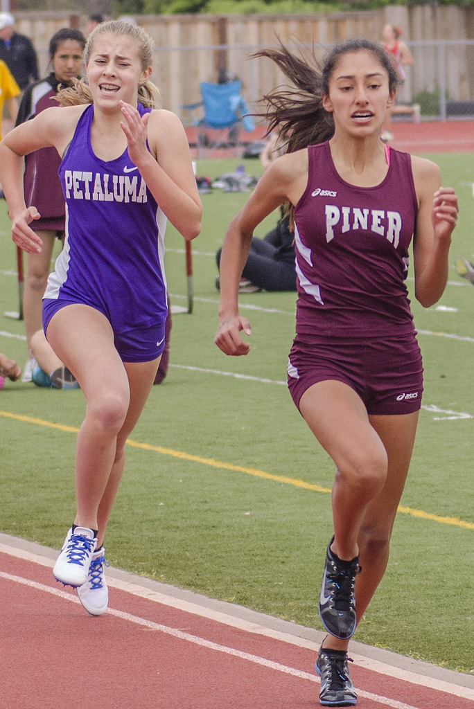 Athlete prepares for pole vault on a track with others watching.