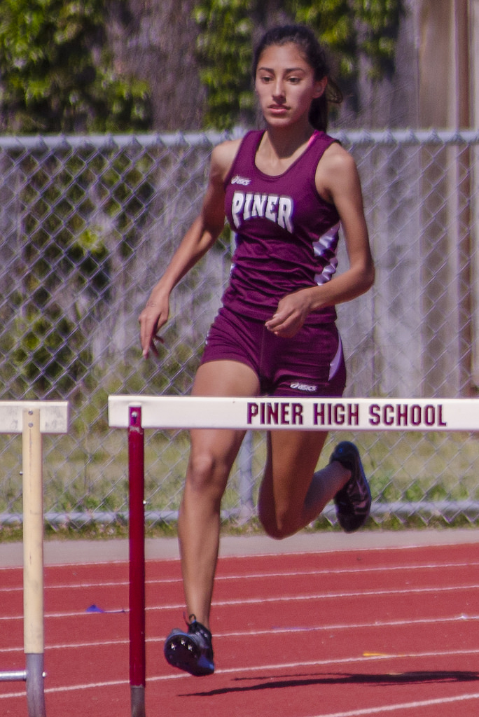 Athlete prepares for pole vault on a track with others watching.