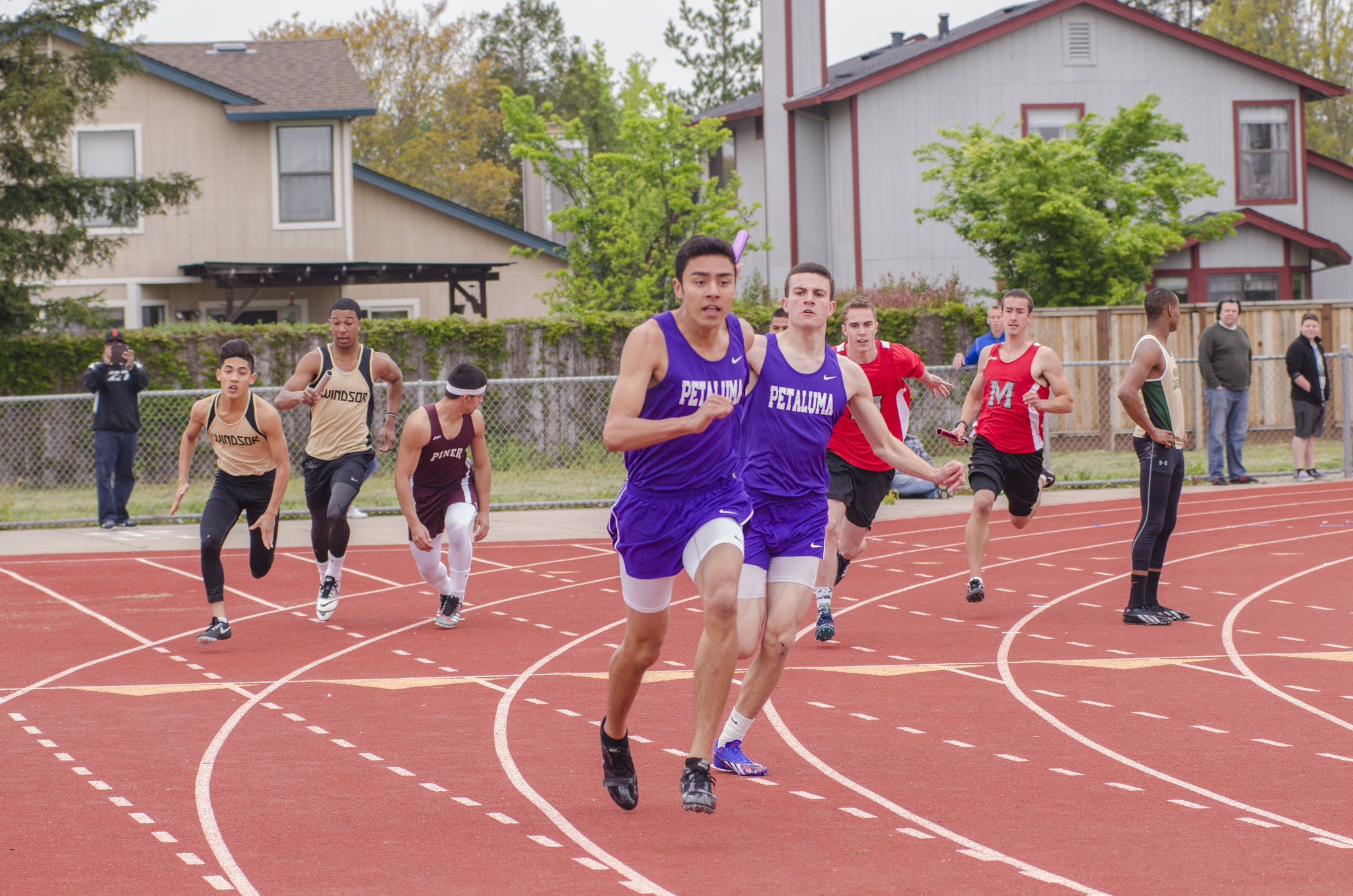 Athlete prepares for pole vault on a track with others watching.