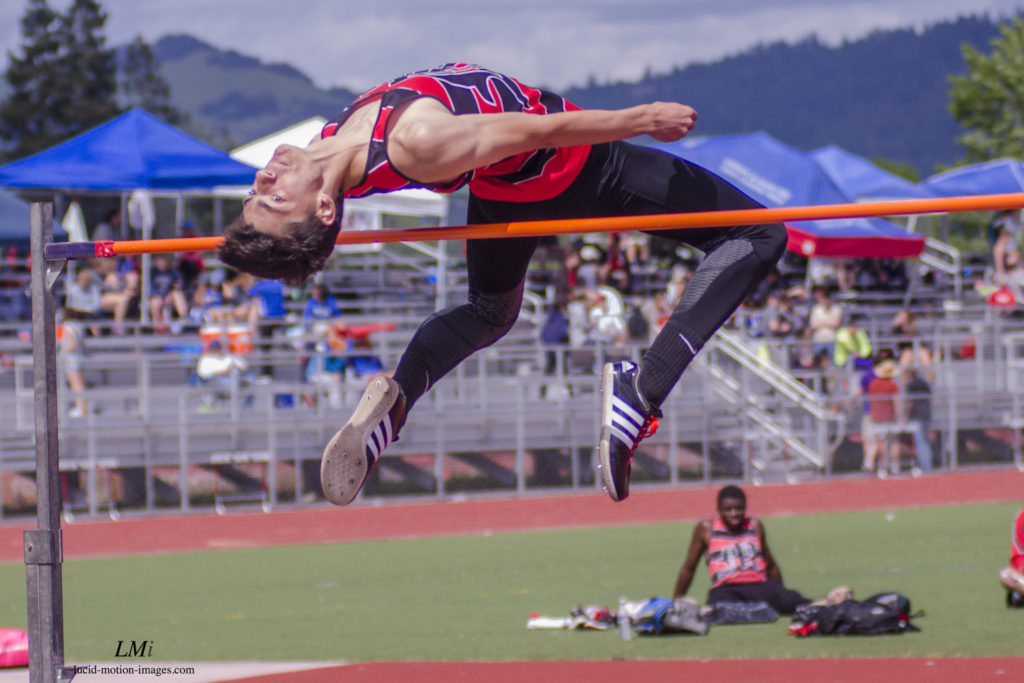 Athlete prepares for pole vault on a track with others watching.