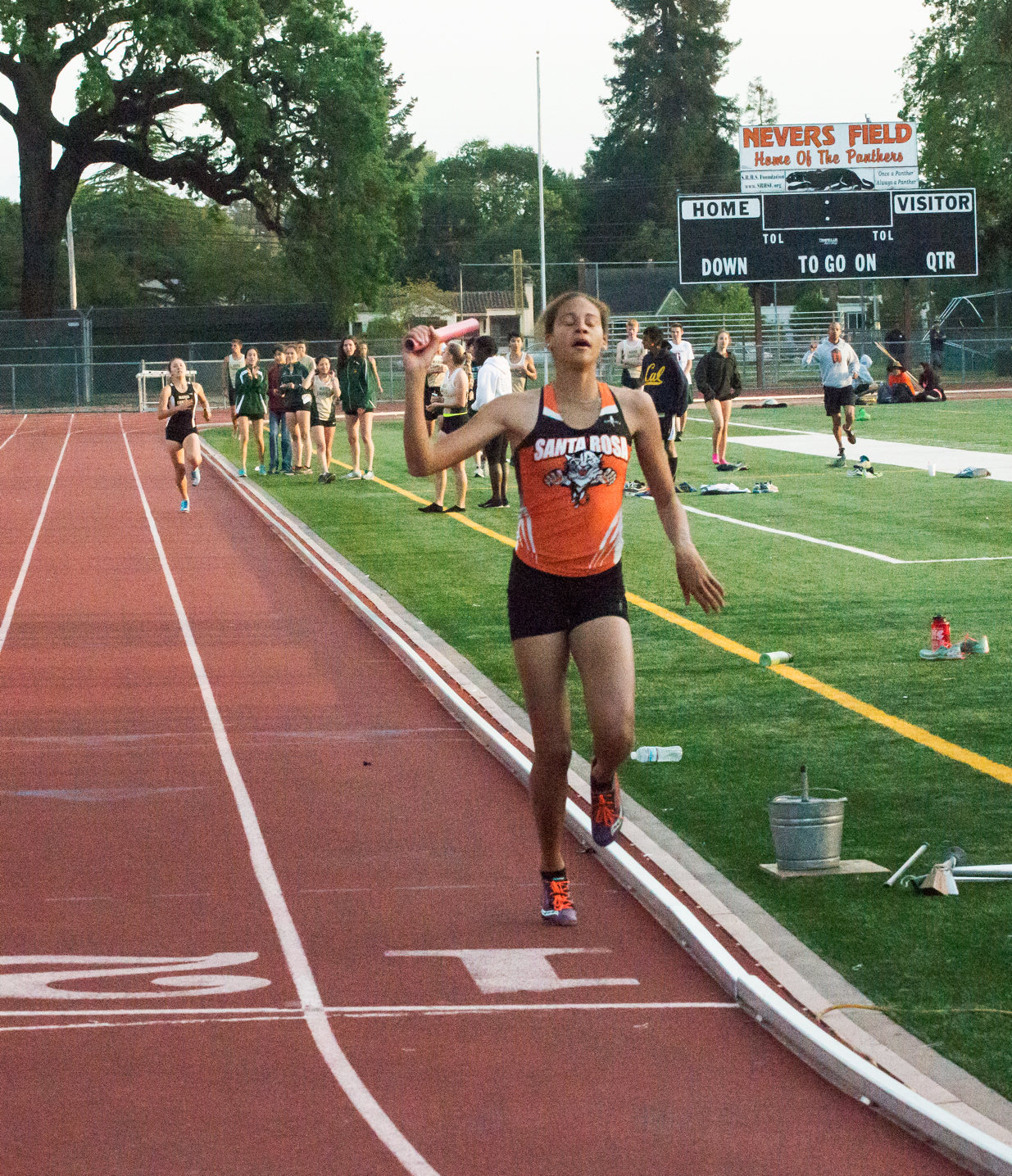 Athlete prepares for pole vault on a track with others watching.