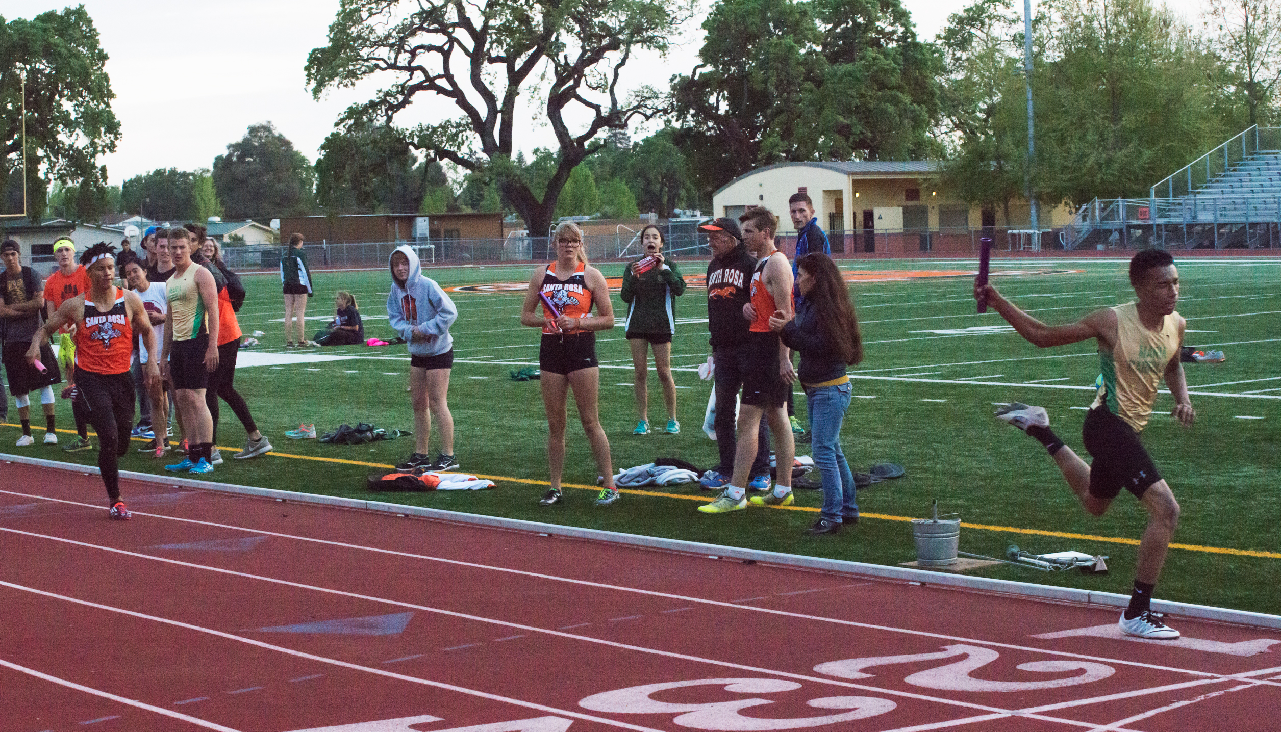 Athlete prepares for pole vault on a track with others watching.