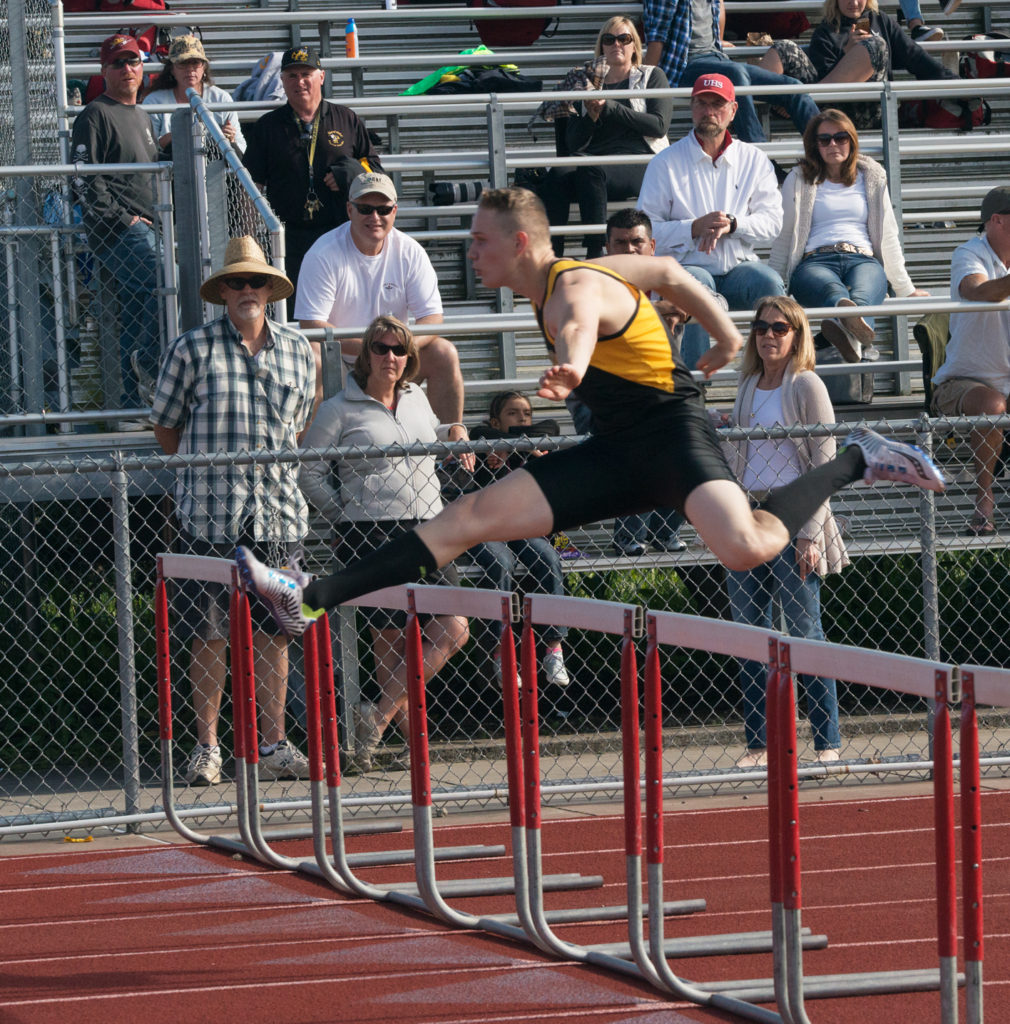 Athlete prepares for pole vault on a track with others watching.