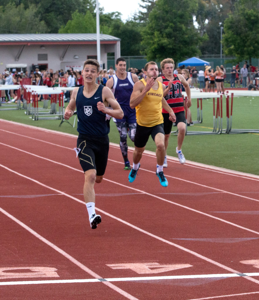 Athlete prepares for pole vault on a track with others watching.