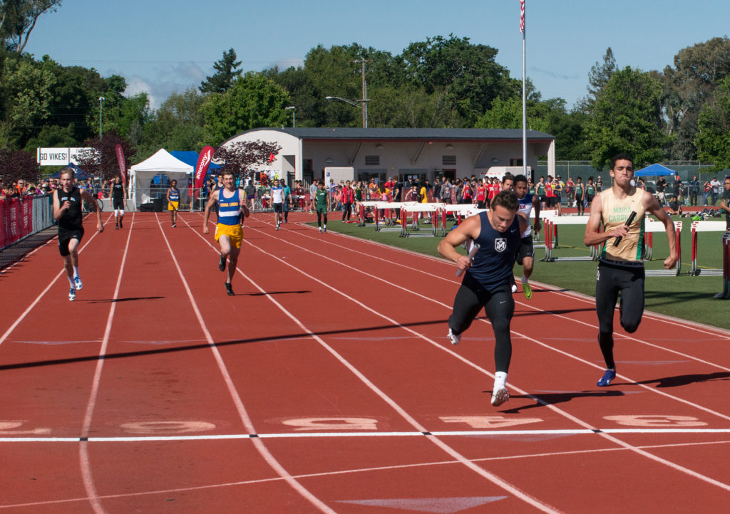 Athlete prepares for pole vault on a track with others watching.