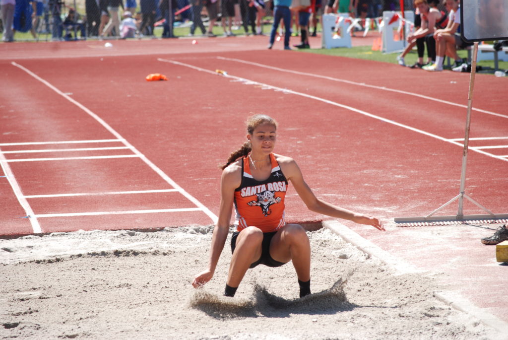 Athlete prepares for pole vault on a track with others watching.