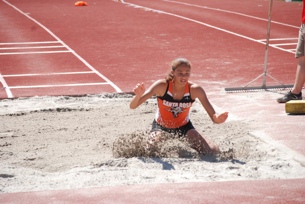 Athlete prepares for pole vault on a track with others watching.