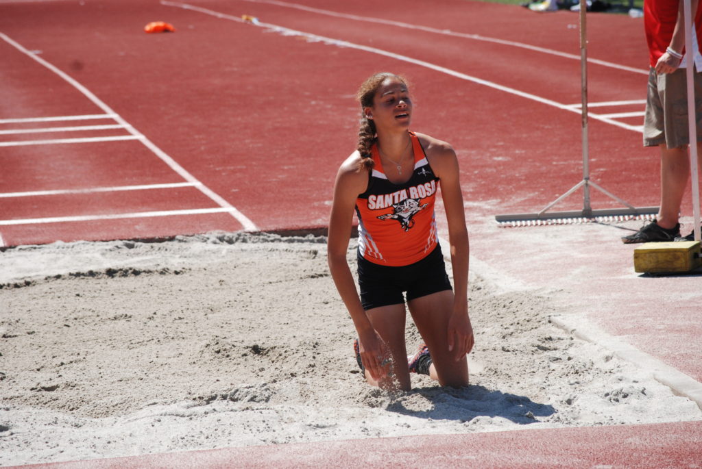 Athlete prepares for pole vault on a track with others watching.