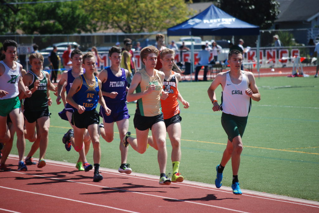 Athlete prepares for pole vault on a track with others watching.
