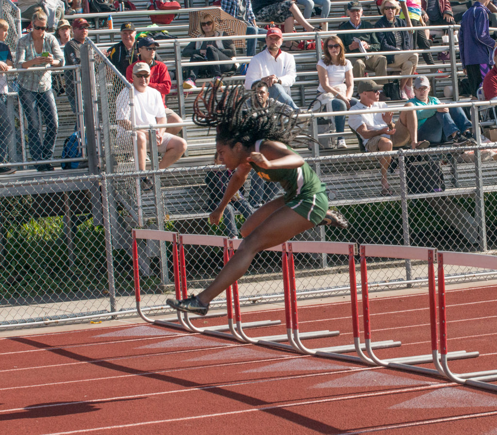 Athlete prepares for pole vault on a track with others watching.