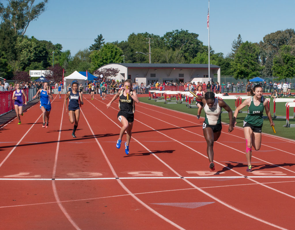 Athlete prepares for pole vault on a track with others watching.