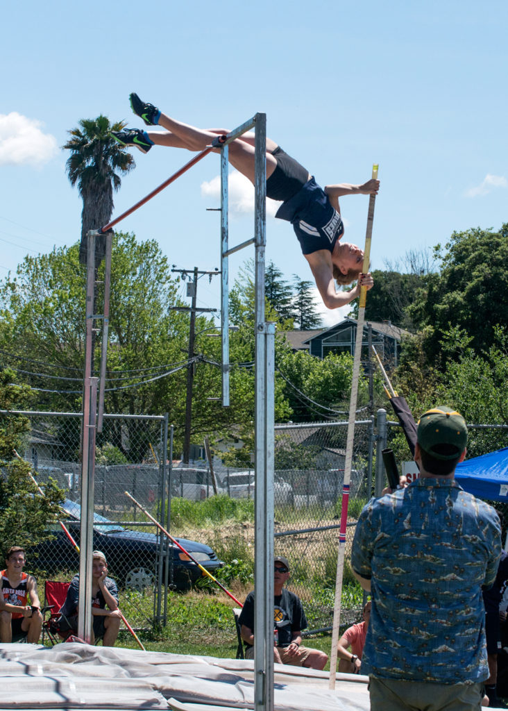 Athlete prepares for pole vault on a track with others watching.