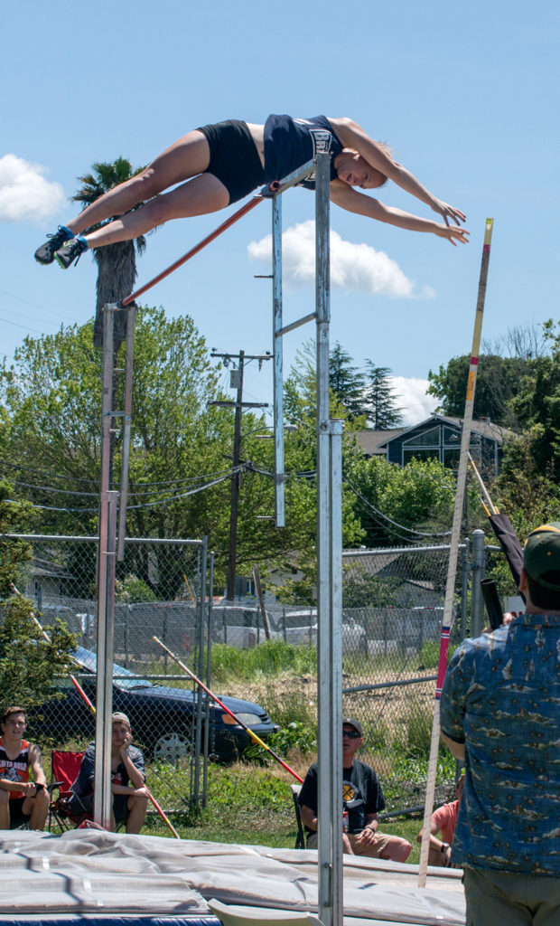 Athlete prepares for pole vault on a track with others watching.