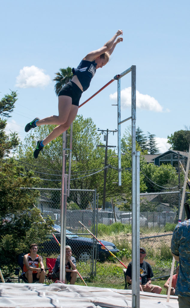 Athlete prepares for pole vault on a track with others watching.