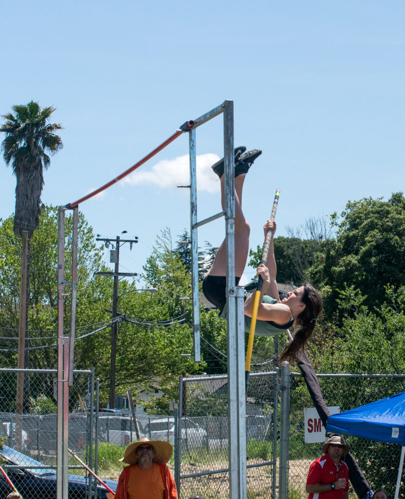 Athlete prepares for pole vault on a track with others watching.