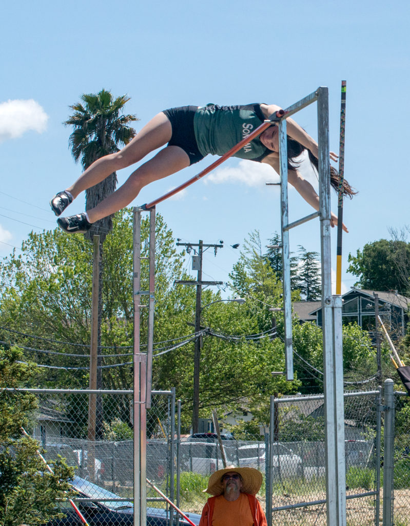 Athlete prepares for pole vault on a track with others watching.