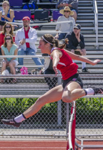 Athlete prepares for pole vault on a track with others watching.