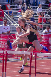 Athlete prepares for pole vault on a track with others watching.