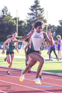 Athlete prepares for pole vault on a track with others watching.