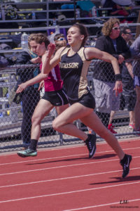 Athlete prepares for pole vault on a track with others watching.