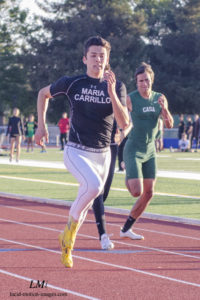 Athlete prepares for pole vault on a track with others watching.