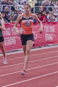 Athlete prepares for pole vault on a track with others watching.
