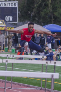 Athlete prepares for pole vault on a track with others watching.