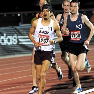 Athlete prepares for pole vault on a track with others watching.