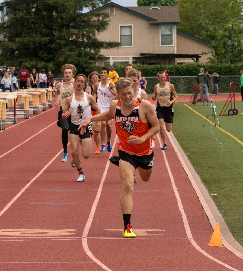 Athlete prepares for pole vault on a track with others watching.