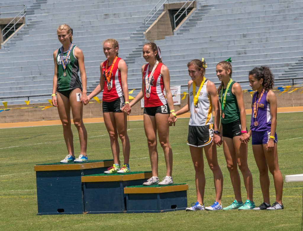 Athlete prepares for pole vault on a track with others watching.