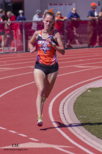 Athlete prepares for pole vault on a track with others watching.