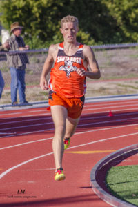 Athlete prepares for pole vault on a track with others watching.