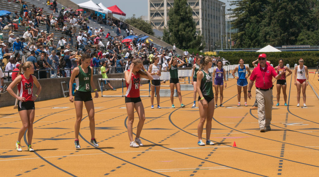 Athlete prepares for pole vault on a track with others watching.