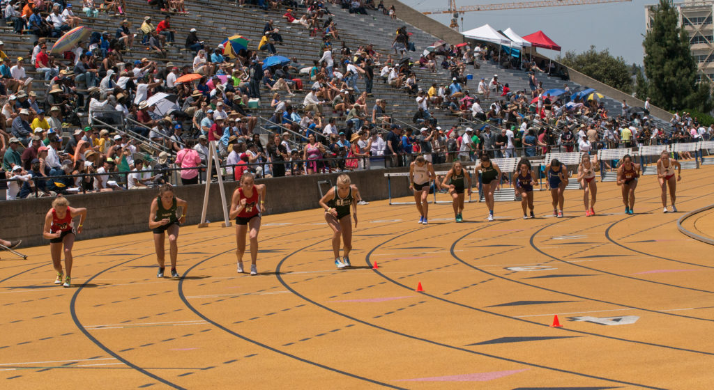 Athlete prepares for pole vault on a track with others watching.