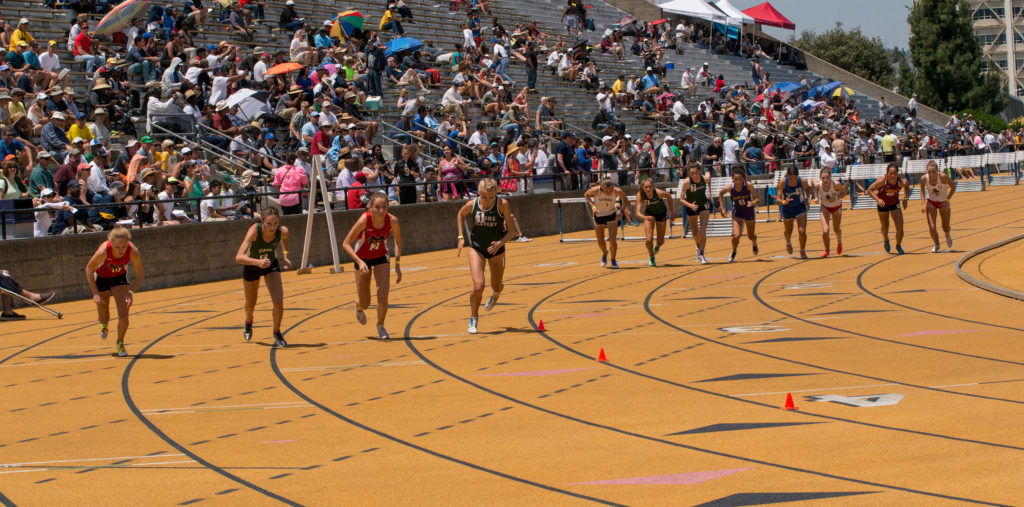 Athlete prepares for pole vault on a track with others watching.