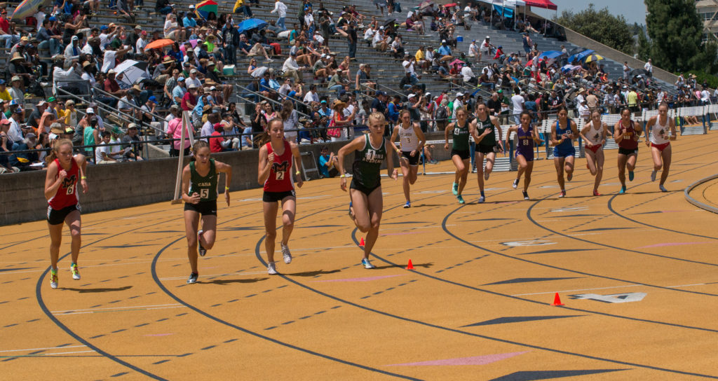 Athlete prepares for pole vault on a track with others watching.